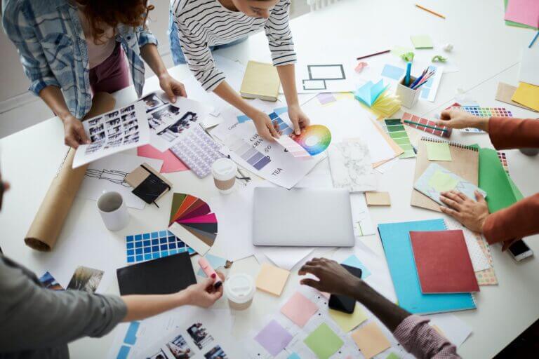 processo de brainstorming entre colaboradores: mesa cheia de papéis brancos e coloridos, cartela de cores, canetas